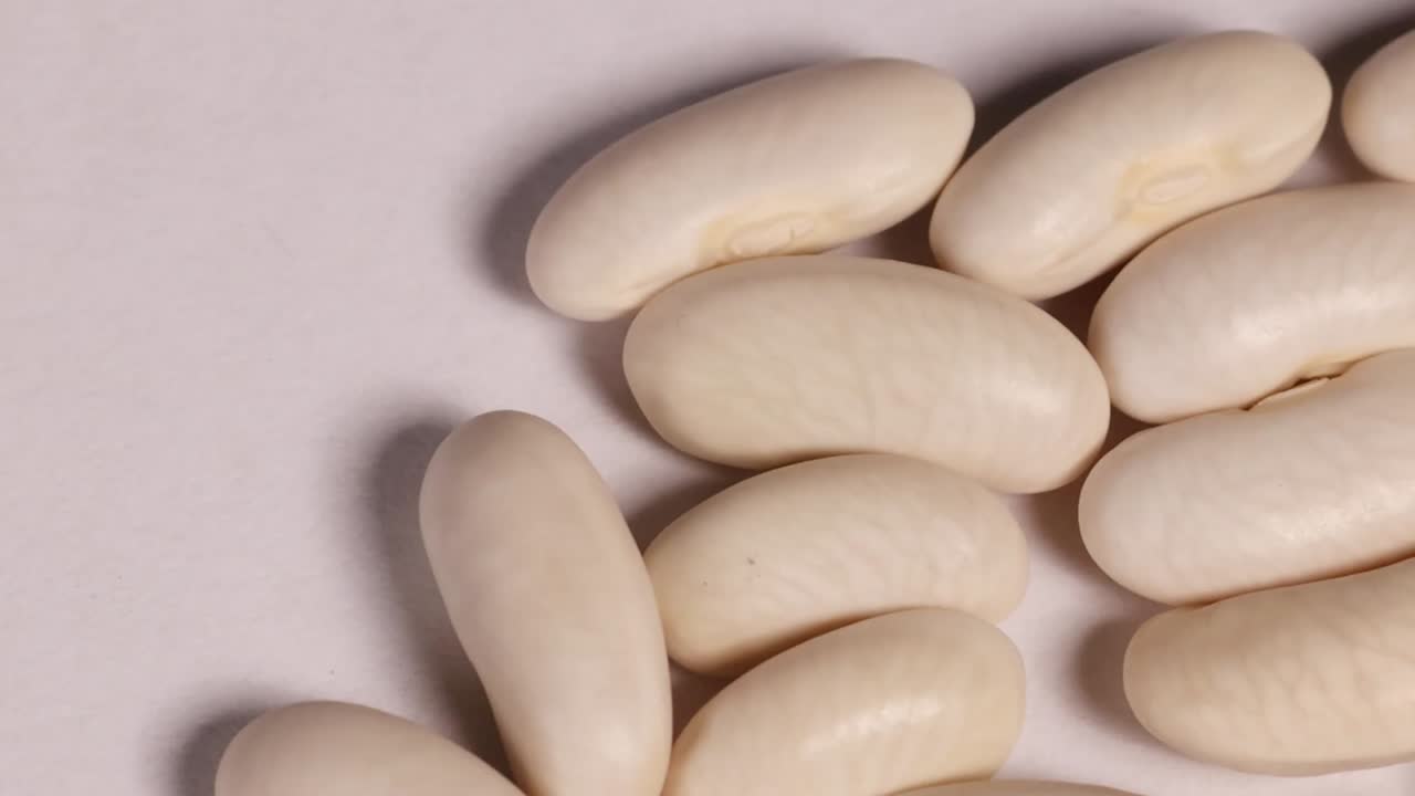 Vue macro extrême de graines de haricots blancs éparpillées, présentant des textures lisses et des formes organiques