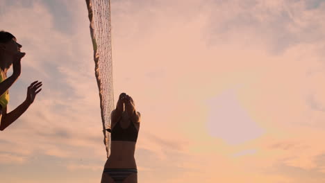 slow motion low angle close up sun flare: athletic girl playing beach volleyball jumps in the air and strikes the ball over the net on a beautiful summer evening. caucasian woman score a point.