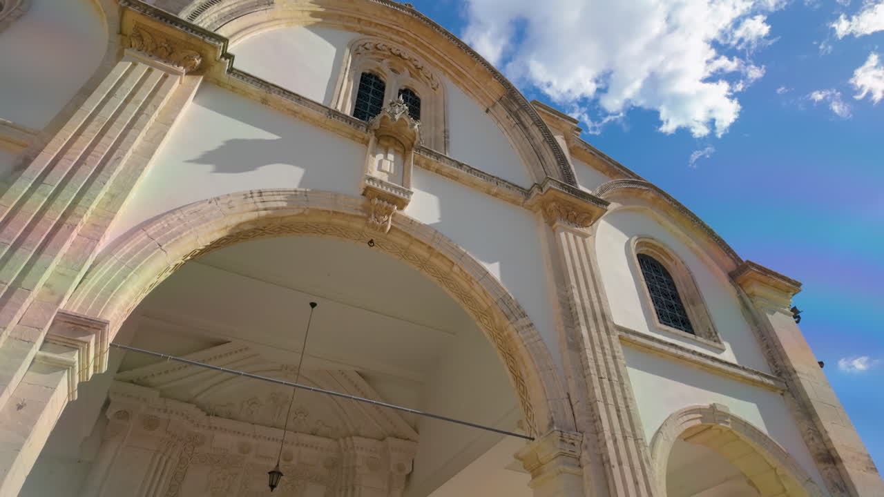 레프카라에 있는 한 교회 앞면은 고전적인 건축 요소와 아치 모양의 입구로, 푸른 하늘을 배경으로 빛으로 여 있다.