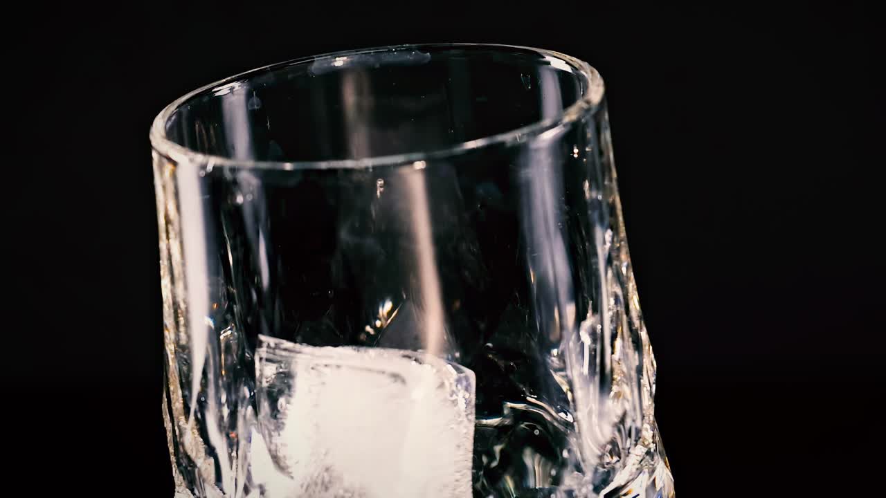 A close-up view of an ice cube tilting inside a transparent glass against a dark backdrop.