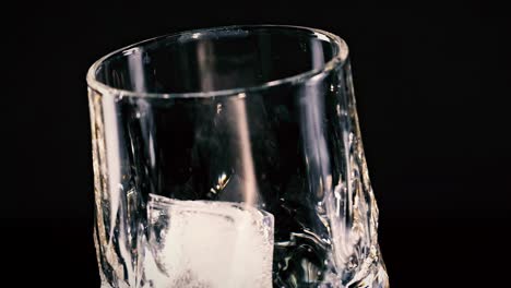 a close-up view of an ice cube tilting inside a transparent glass against a dark backdrop.