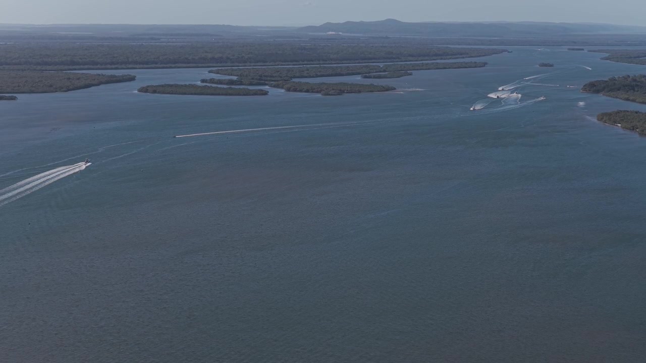 Perahu-perahu meninggalkan jejak putih melintasi saluran pesisir dekat Pulau Coomera di Queensland, Australia. Pemandangan udara luas.