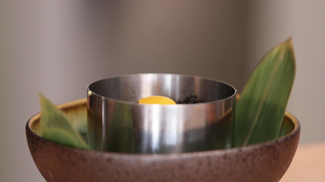 chef poniendo huevo de codorniz encima del tartar de atún dentro del moldeador de acero inoxidable