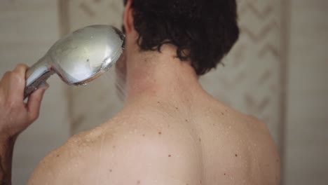 white man with dark hair washes his neck with the shower head in his hand