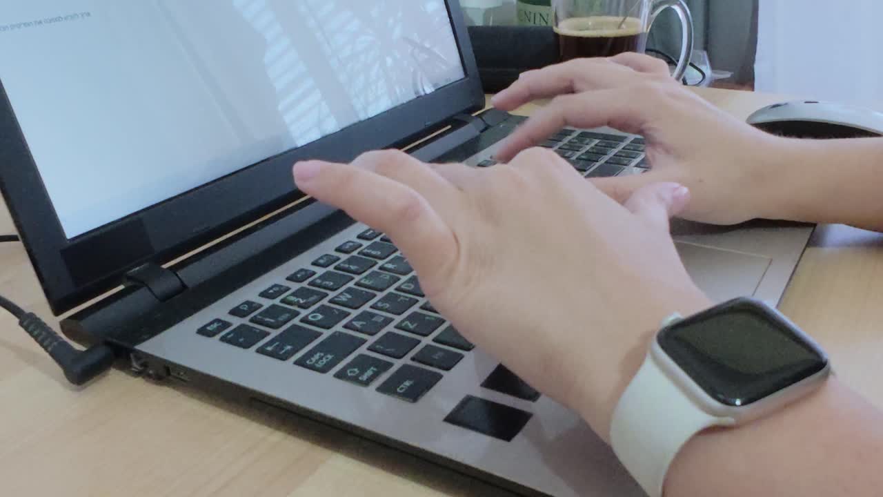 Person working remotely, hands typing on laptop at a home office desk with coffee and smartwatch.