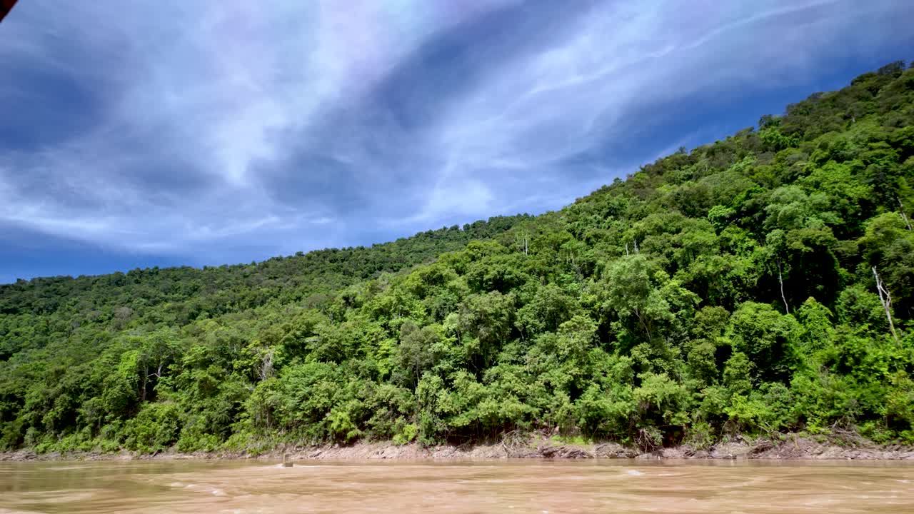 O rio Mekong flui ao lado de uma encosta arborizada sob um céu nublado