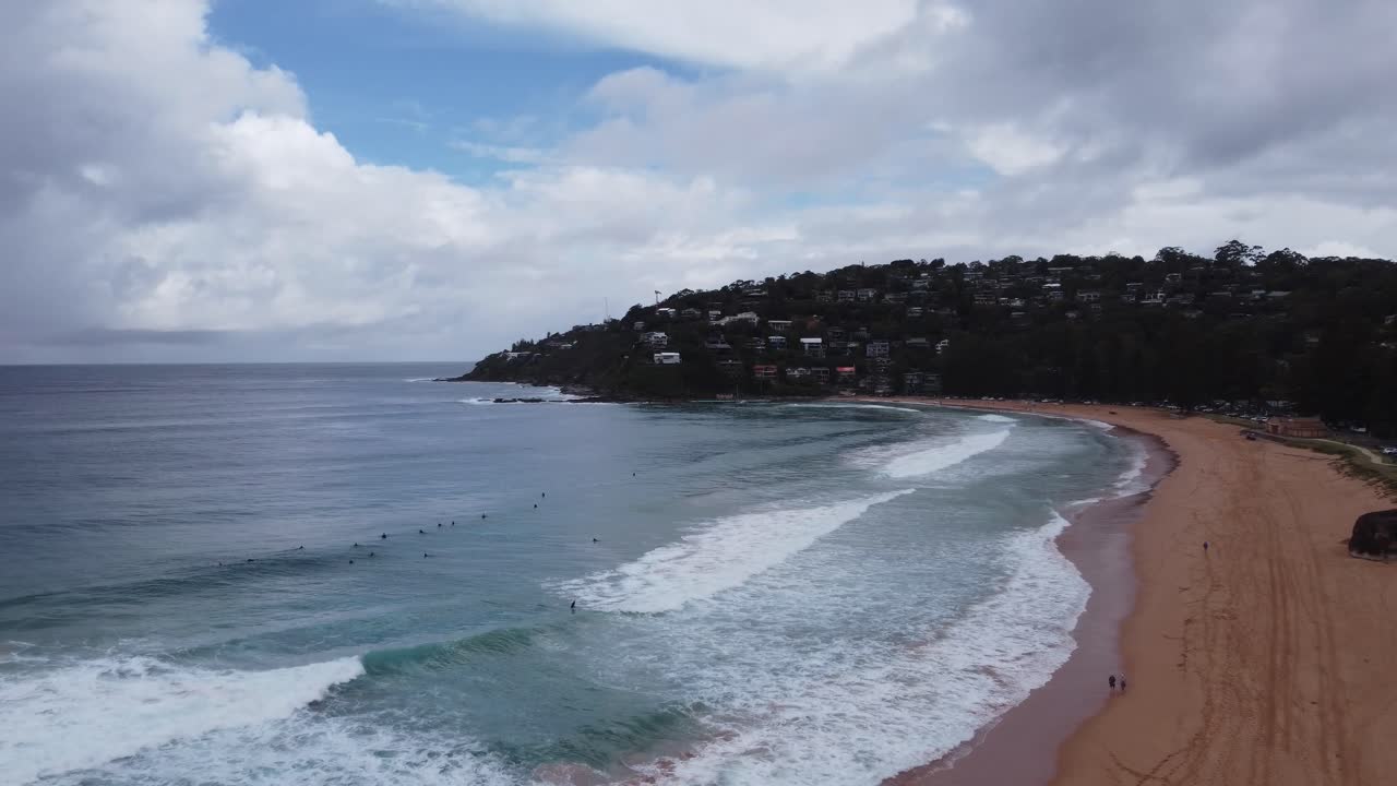 drone volando hacia los surfistas en una hermosa playa de surf en un día nublado
