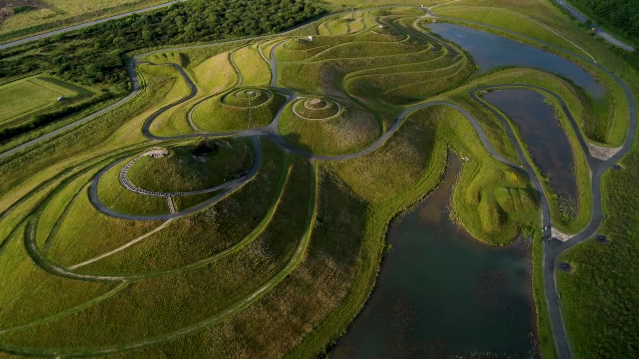 Aerial drone footage capturing circular winding roads on green agricultural hills in England, UK, showcasing terraced farmland and lush vegetation