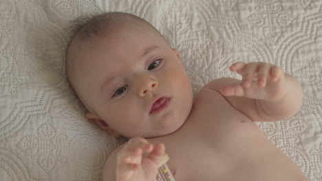 baby laying on his back playing with toy in white bed sheets, bright bedroom