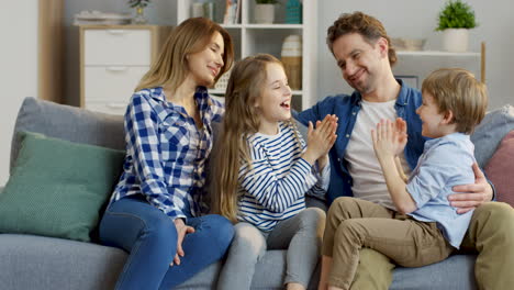 cute little kids, boy and girl, sitting on the knees of their mother and father and playing a hand game