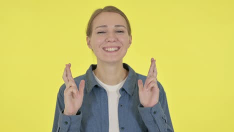 young woman praying with fingers crossed on yellow background