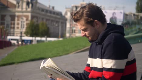 handsome young man sitting near by stedelijk museum in amsterdam concentrated reading a book. netherlands. flat plane close up