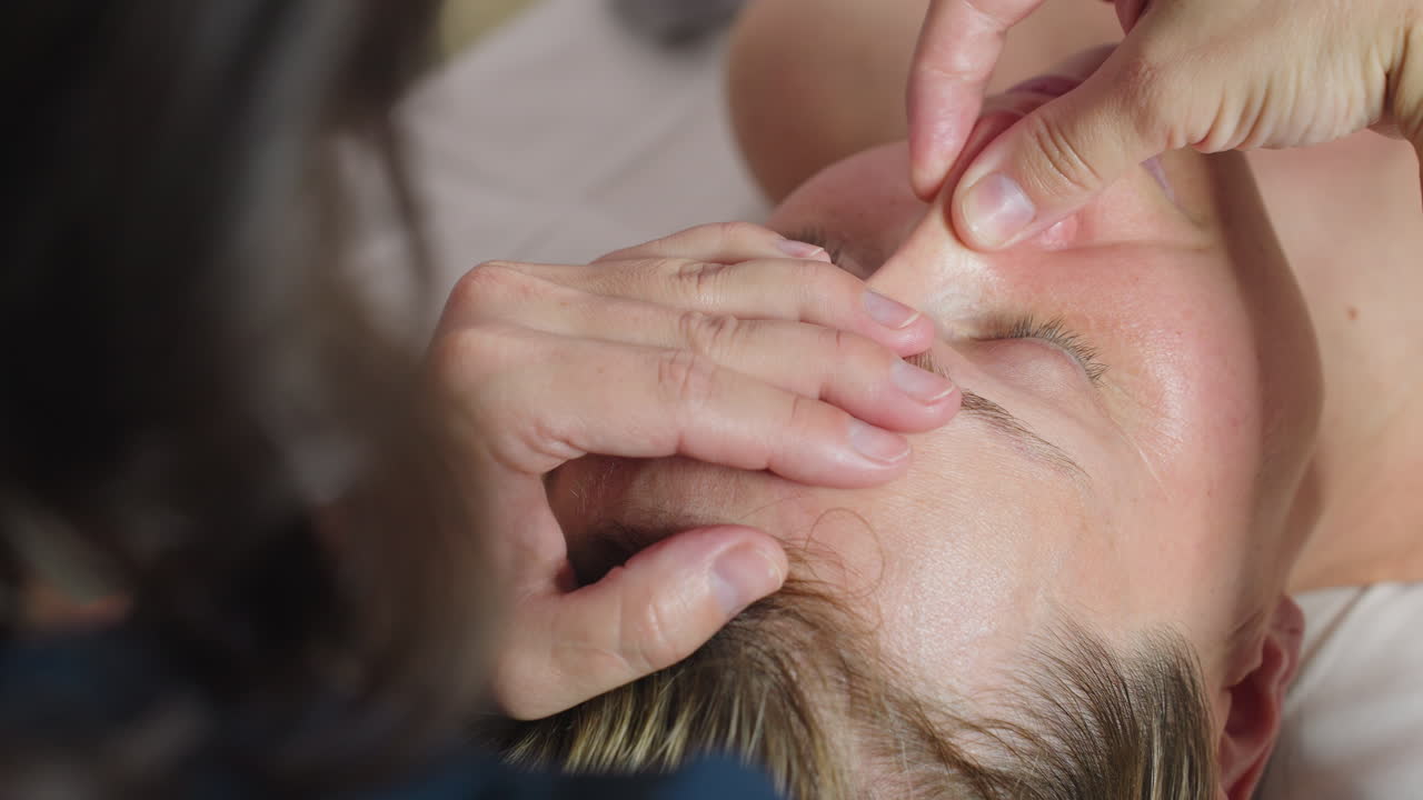 Wellness technician sprays hands with lightweight hydration mist then rubs palms together prepping skin for facial treatment under soft clinical lighting in spa environment with sanitary prep