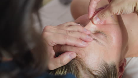 wellness technician sprays hands with lightweight hydration mist then rubs palms together prepping skin for facial treatment under soft clinical lighting in spa environment with sanitary prep