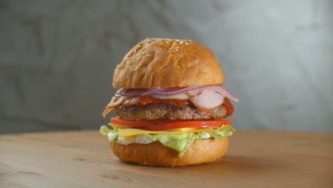 great burger with beef cutlet tomatoes mushrooms and cucumbers with melted cheese rotates on a wooden board on light background.