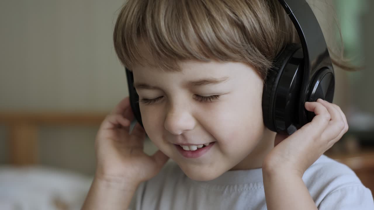 портрет милого маленького мальчика с наушниками, слушающего музыку. медленное движение ребенка на расслаблении с закрытыми глазами в наушниках. ребенок слушает музыку дома. веселое беззаботное детство.