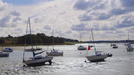 handheld shot of a pair of boats with many more in the background at low tide in a river in the mud