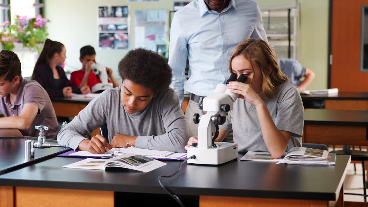 estudiantes de secundaria con tutor usando el microscopio en la clase de biología