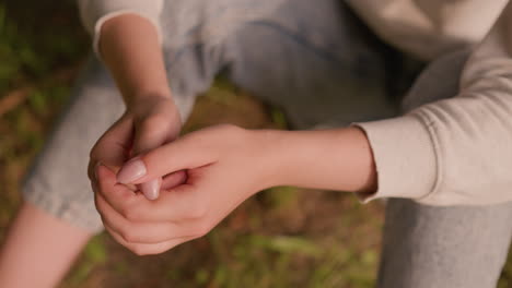 close-up of individual hands clasped together in a calm, reflective pose been rub gently, resting on knees with soft background of autumn foliage on ground