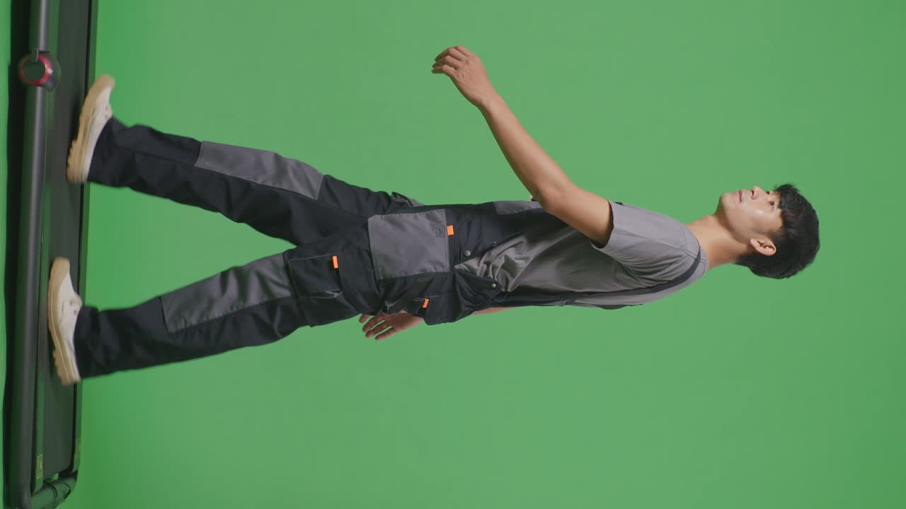 으로 보기: 아시아 남성 노동자의 전체 몸체가 녹색 스크린 배경 스튜디오에서 걸어서 주위를 둘러보고 있습니다.