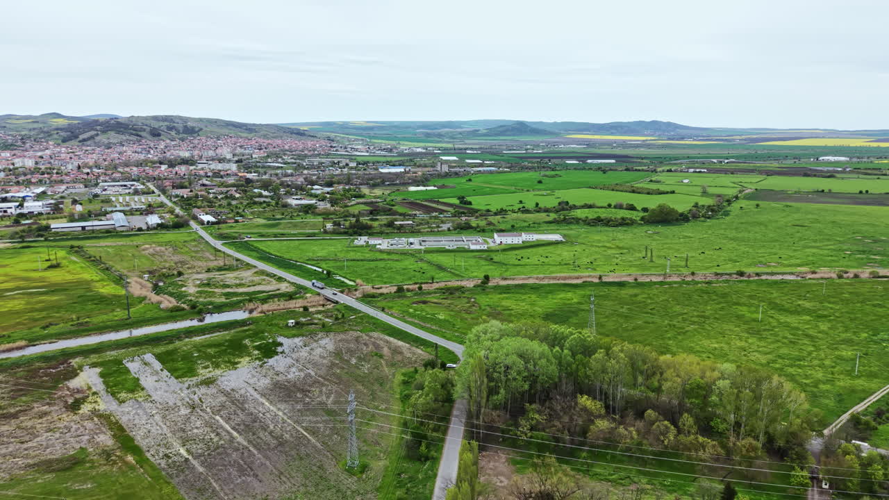 Vista a volo d'uccello di campi verdi e area urbana con colline in lontananza vicino a una piccola città.