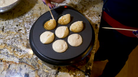 ebelskivers being cooked and turned with a wooden stick in an electric dutch oven