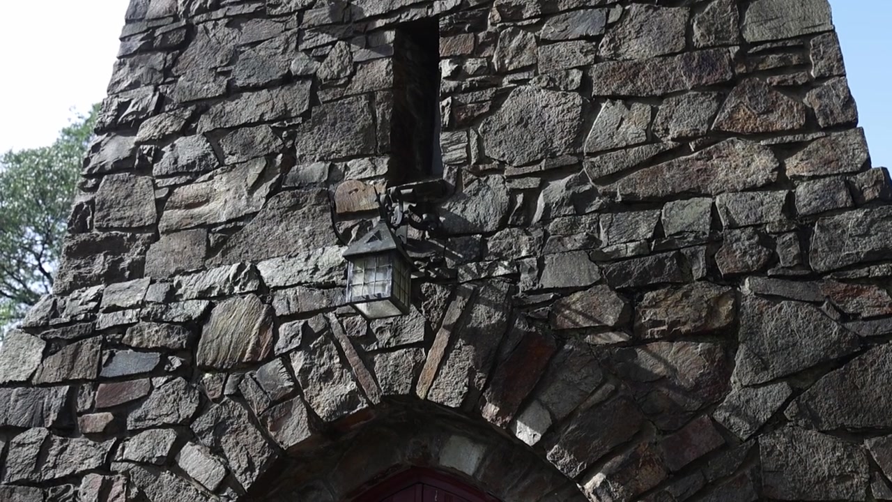 Imagem estática em close-up da fachada de pedra robusta e entrada em arco de uma antiga igreja de Olinda em Melbourne, realçada pela luz natural do dia e detalhes arquitetónicos rústicos.