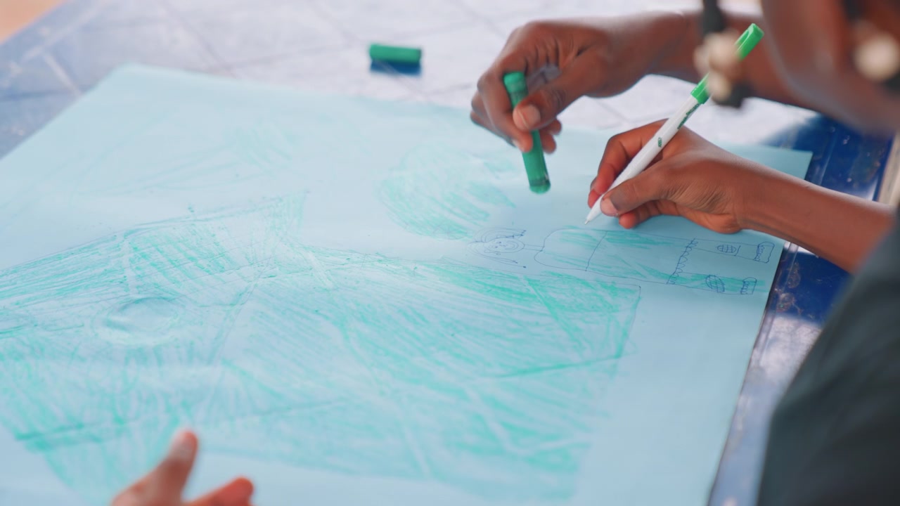 Madre e figlio che disegnano con i pastelli su carta blu, mani in primo piano mentre il genitore guida i tratti, morbidi scarabocchi color verde acqua, un delicato momento di insegnamento, pratica della motricità fine, scena di legame artistico in casa.