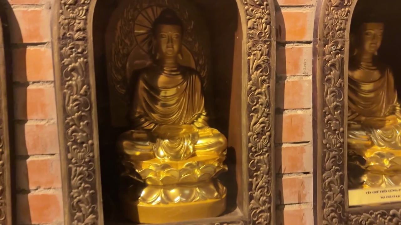 Corridoio del tempio nella Pagoda di Bai Dinh a Ninh Binh, Vietnam, caratterizzato da pareti in mattoni rivestite con nicchie ad arco in vetro contenenti piccole statue dorate di Buddha