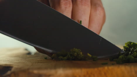 primer plano de una mano masculina cortando cebolletas en una tabla de cortar de madera en un ambiente de cocina ahumado
