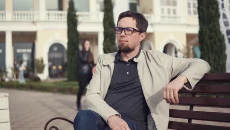 a man in glasses in his eyes sits on a bench and resting in the fresh air