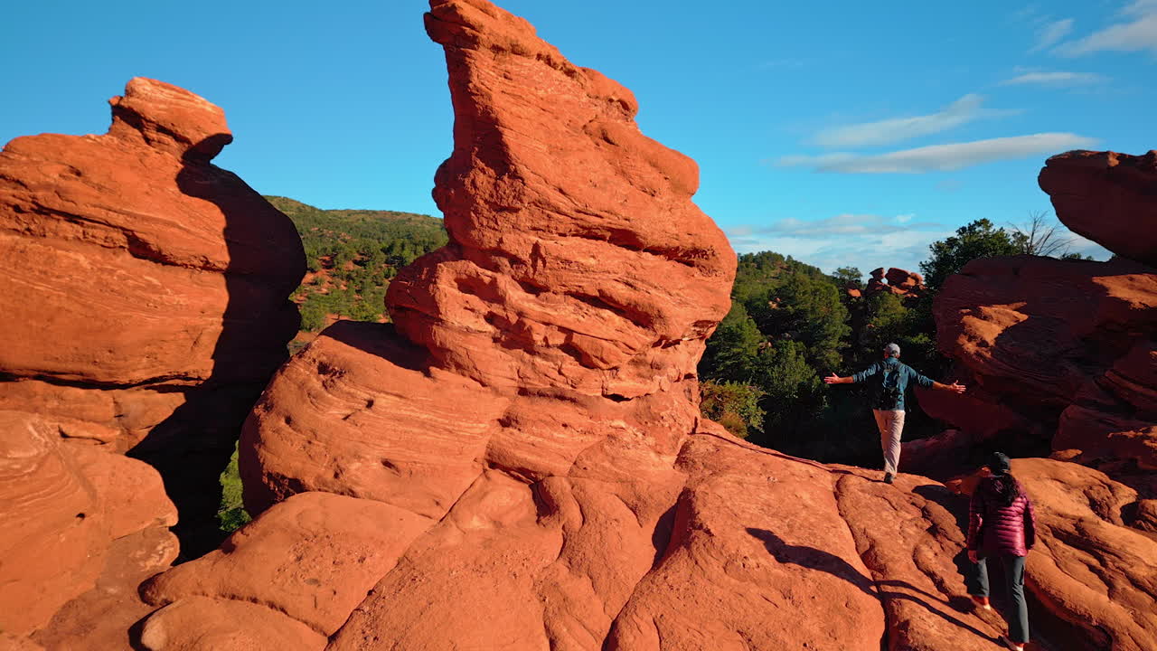 Stunning red rocks lit by the bright sun. A couple walks by the rock formations of Garden of the Gods Park, Colorado Springs, Colorado, USA