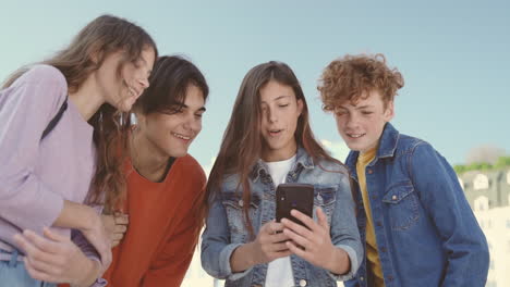 un grupo de adolescentes con dos chicas y dos chicos viendo algo en la pantalla de un teléfono móvil 4