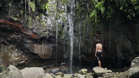 panorámica hasta el hombre en la roca contemplando una pequeña cascada en la jungla floreciente