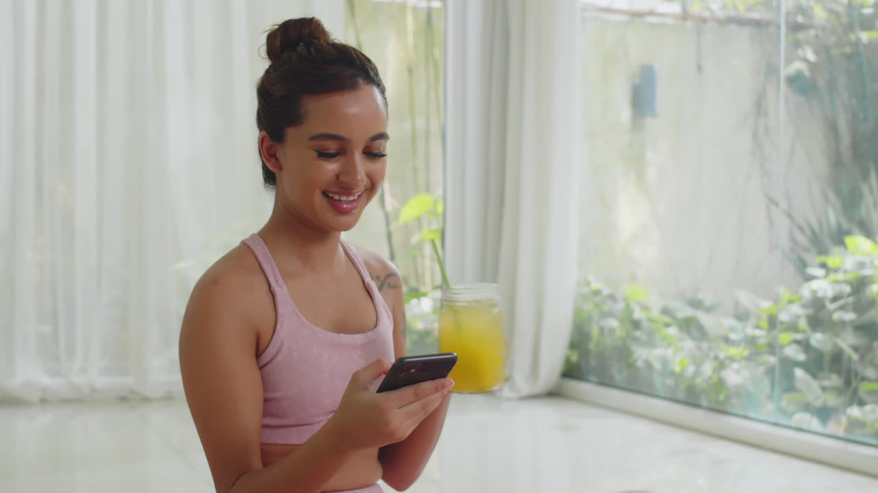 Sportswoman Scrolling Feed on Phone and Drinking Lemonade after Home Training