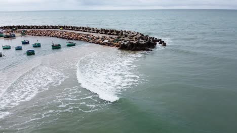 Drone-flyover-lonely-Surfer-floating-waiting-for-waves,-Mui-ne-bay-with-traditional-boats-moored,-Vietnam