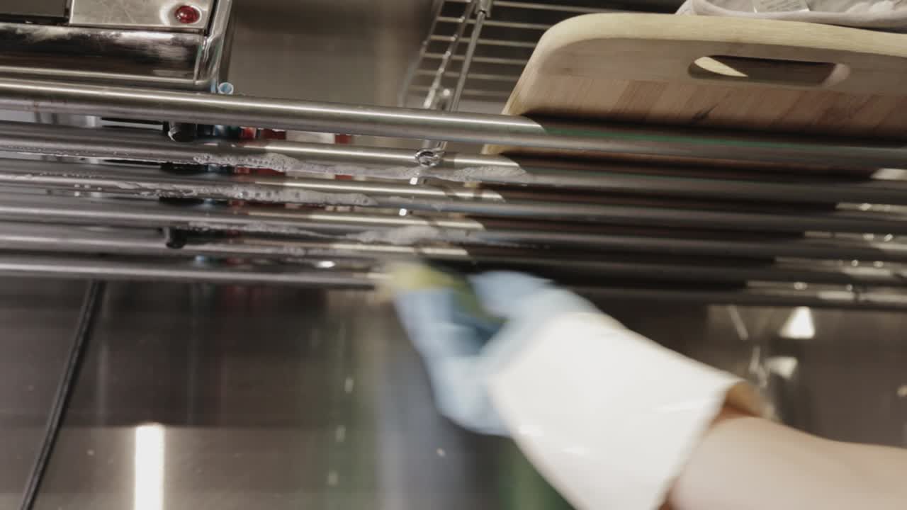 Cleaning The Kitchen Stainless Steel Over-The-Sink Rack Drainer With A Wet Soapy Sponge - Close Up Shot
