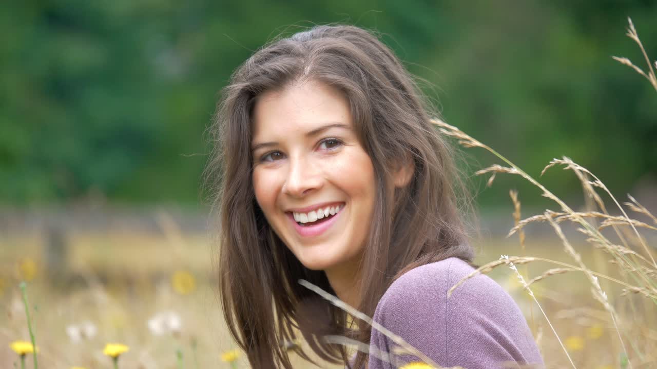 Hermosa joven ríe felizmente mientras está sentada en un hermoso campo de flores amarillas brillantes.