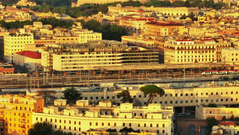 Aerial-shot-of-platform-on-train-station-and-surrounding-buildings-lit-by-bright-morning-sun.-Tilt-up-revealing-famous-ancient-Colosseum.-Rome,-Italy