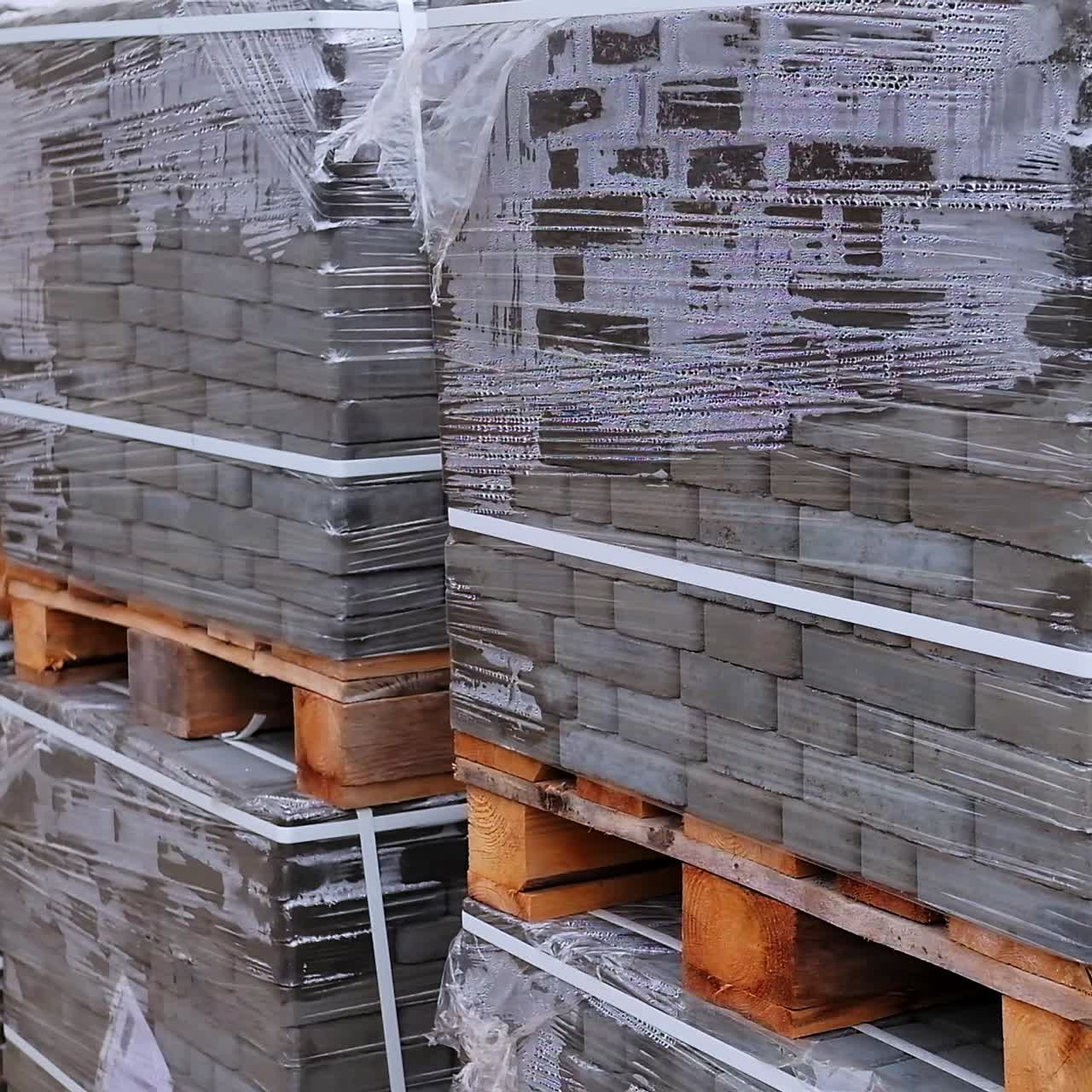Huge packs of grey bricks stacked at wooden pallets. Construction materials covered with cellophane and tied with plastic band