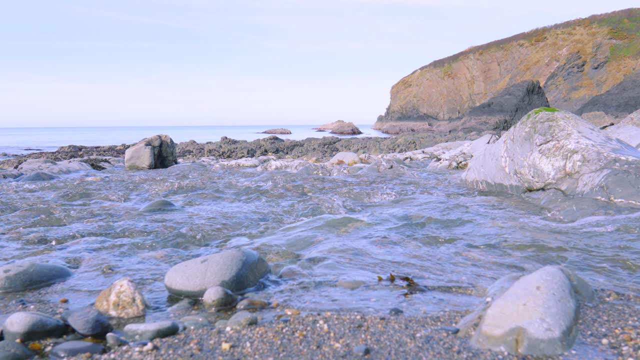 View of Pembrokeshire Rocky Beach as River Flows into Sea with Cliff Coastline. Nature Slow Motion Footage.