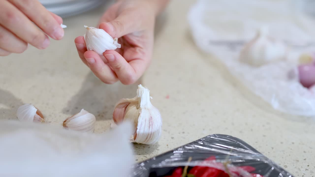 Close-up of hands peeling garlic cloves on a kitchen countertop with natural lighting and a relaxed atmosphere