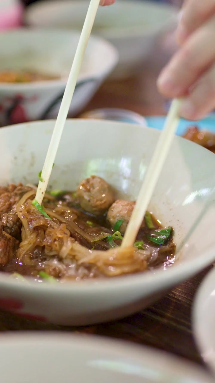 Primer plano de manos usando palillos para comer sopa tradicional tailandesa de fideos con carne de res en un restaurante.
