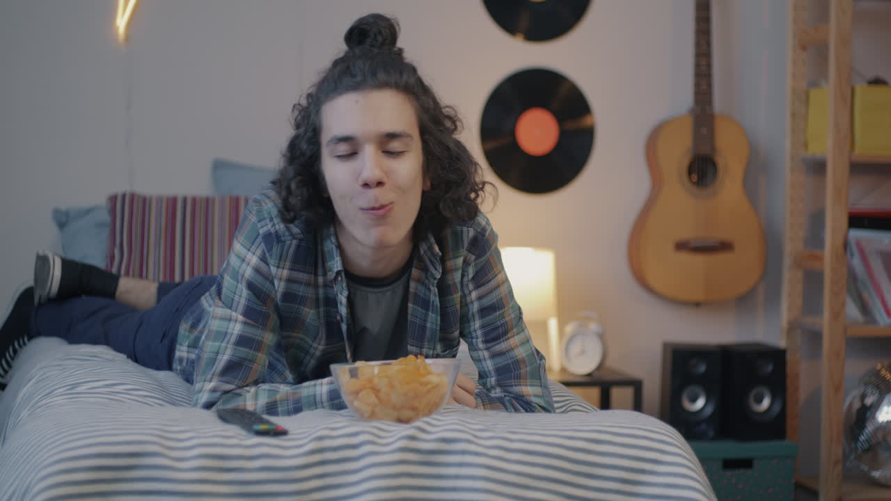 Teenagedreng slapper af og spiser chips på værelset