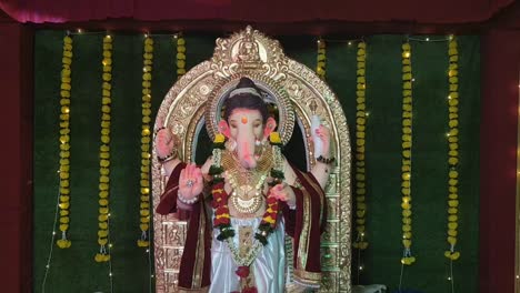 captivating view of lord ganesha statue in pandal, illuminated with vibrant festival lights and set against decorative grass backdrop during ganesh festival.