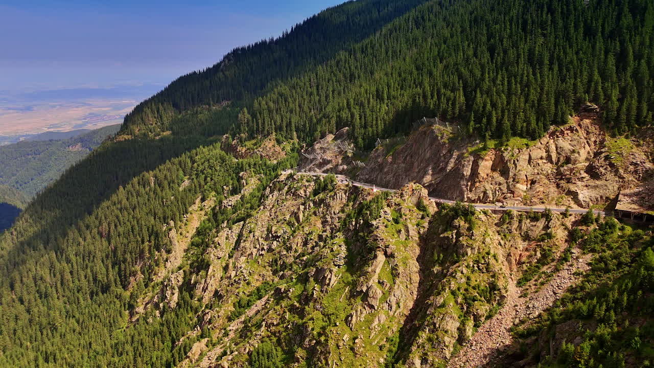 Mountain drive through pines. A winding road cuts through vibrant greenery in a mountainous region under a clear blue sky during midday