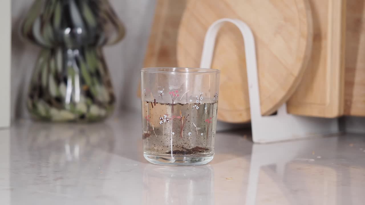 Foglie di tè che si sciolgono in un bicchiere floreale d'acqua sul bancone di una cucina