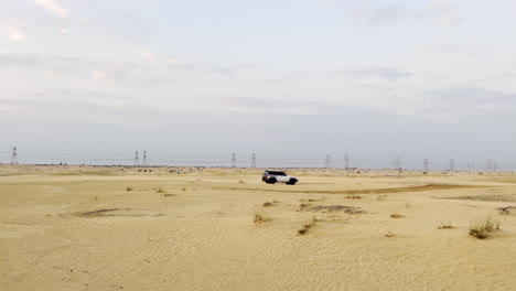 White-SUV-driving-fast-through-the-desert-at-sunset-with-electric-wires-in-the-background