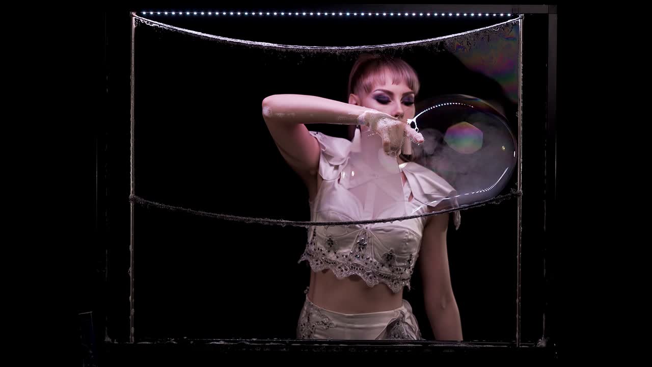 молодая девушка делает трюки с мыльными пузырями. она пробивает один пузырь, дым течет в другой.