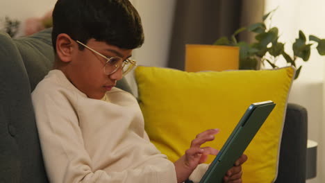 young boy sitting on sofa at home playing games or streaming onto digital tablet 3